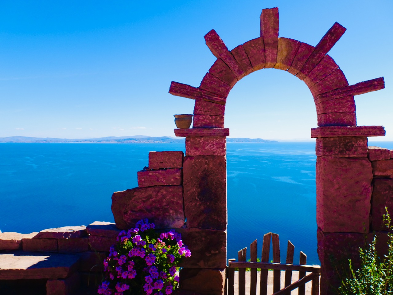 A stone archway framed by flowers overlooking the deep blue water of a far-flung destination
